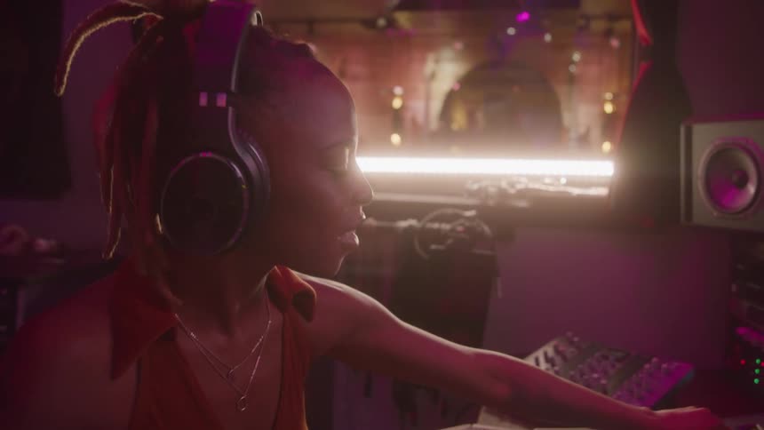 Woman wearing headphones adjusts controls on the mixing console in a studio