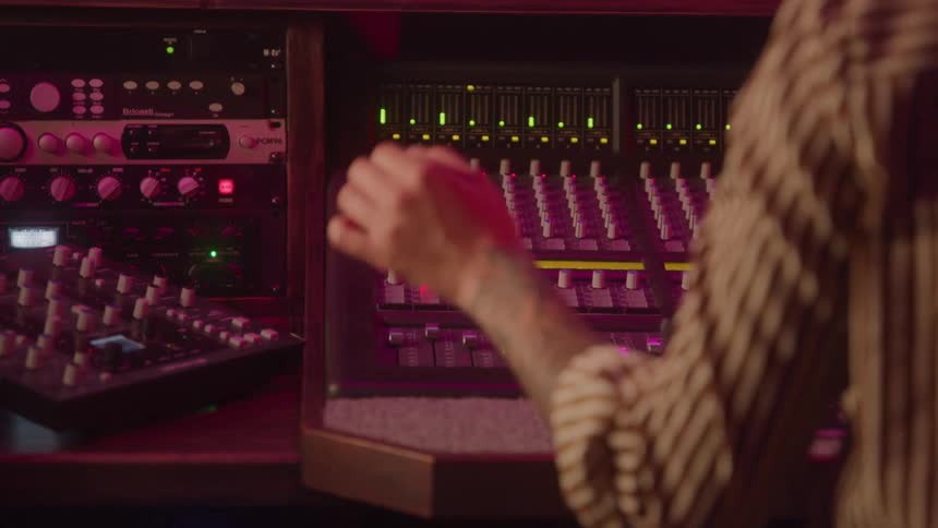 Hand adjusts sliders on the mixing console in a recording studio