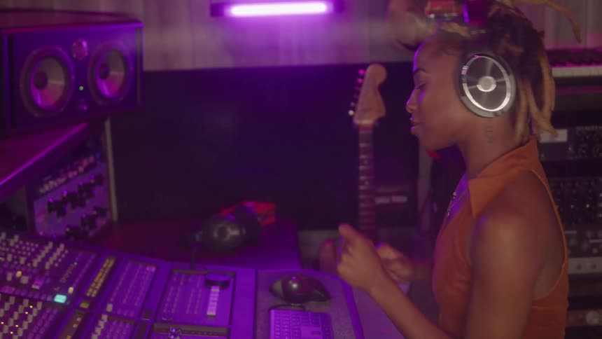 Woman wearing headphones operates controls on the mixing console in a music studio