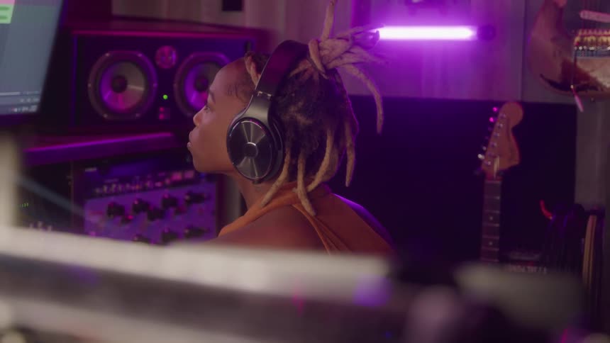 Woman with headphones facing a mixer in a studio