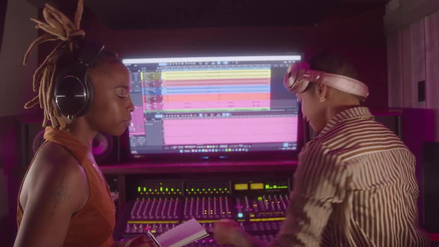 Two women working in a recording studio in front of the mixing console and the screen with editing software