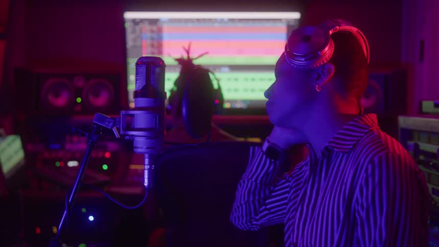 Woman with headphones singing into a microphone in a studio