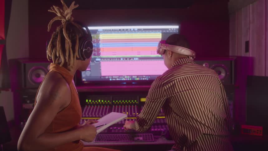 Two people in a recording studio analyzing audio tracks on a screen