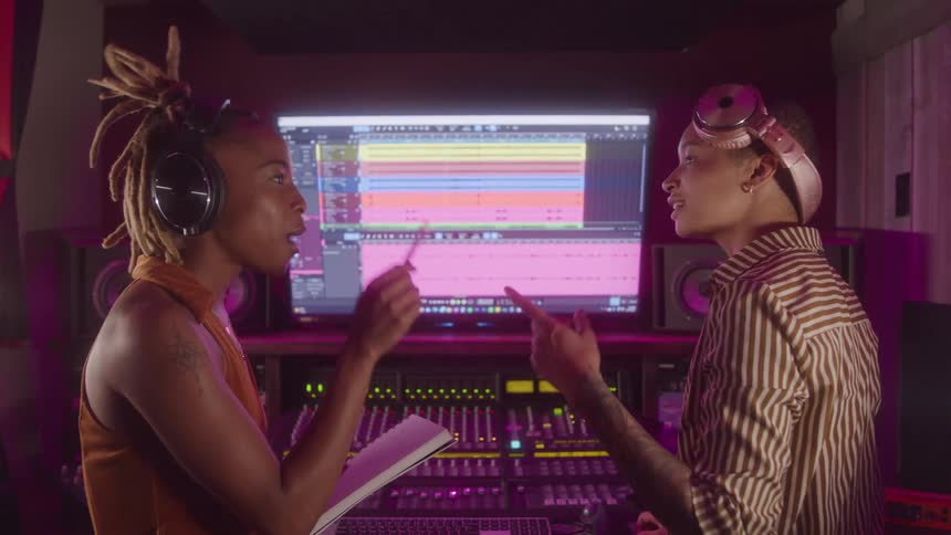 Two people wearing headphones discussing music production in a studio