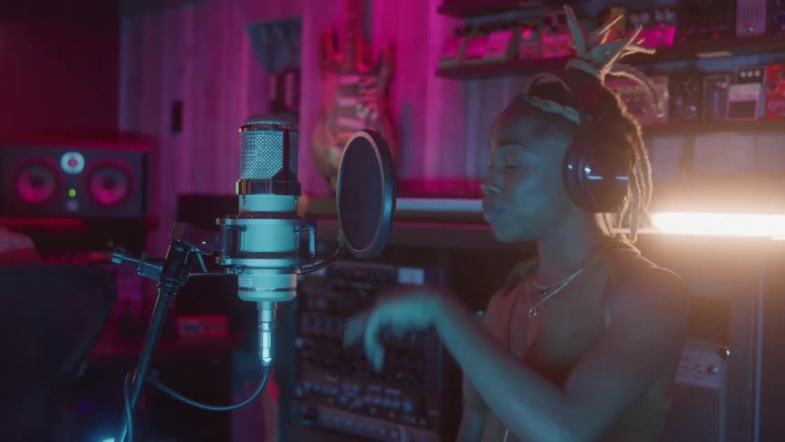 Singer wearing headphones performing in a studio in front of the microphone