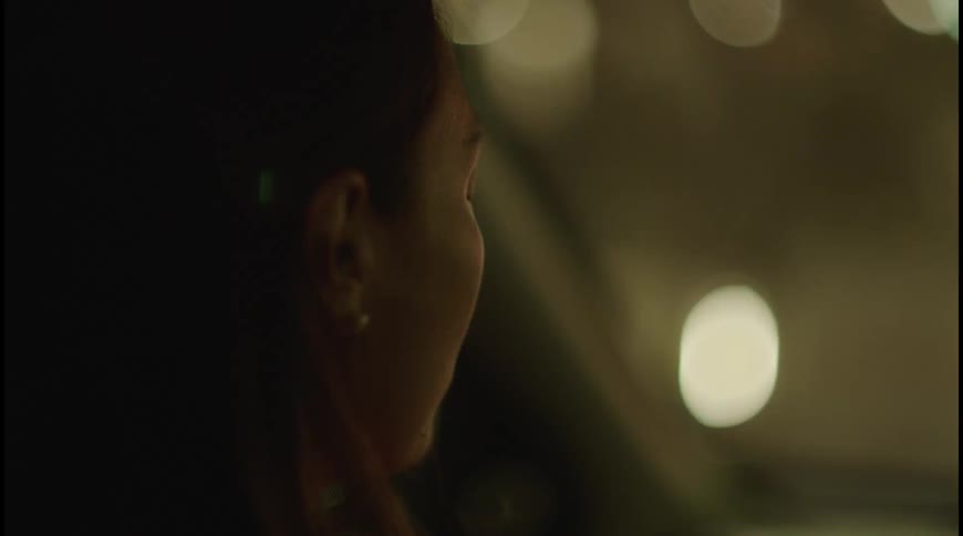 The video shows the profile of a person riding in a car at night the person is looking out the window at the city lights the background is a blur of moving lights from street lamps and other vehicles creating a bokeh effect
