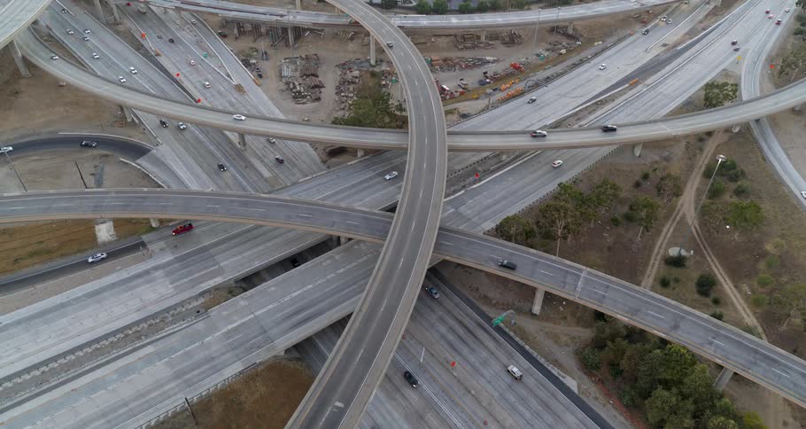 The video shows a busy highway interchange from an aerial perspective cars and large trucks are seen traveling on the multilevel overpasses and the intersecting roads the sky is overcast and the light is flat suggesting a cloudy day