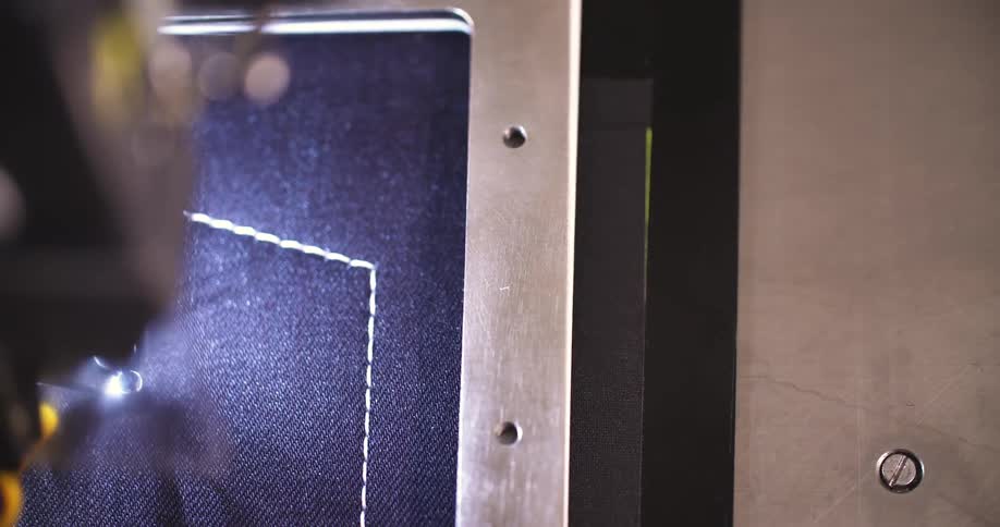 A computerized sewing machine creates a neat rectangular zigzag border on dark fabric under steady guidance