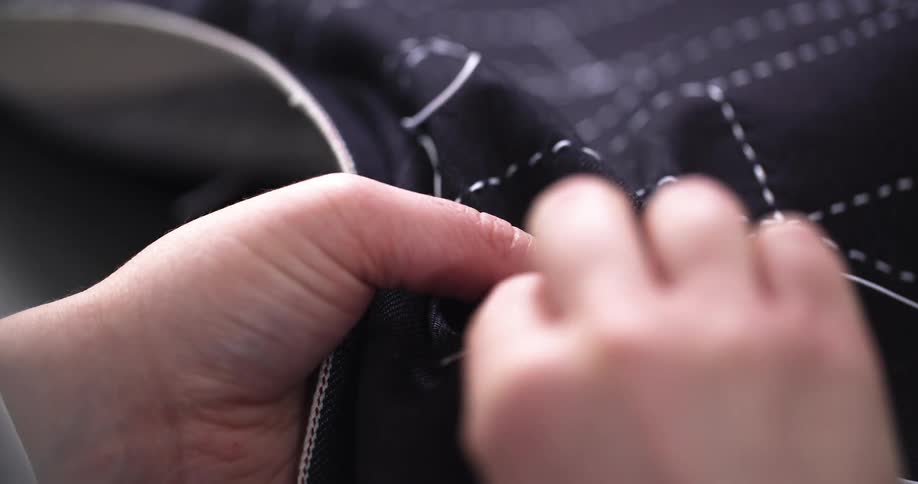 A designer hand stitches white thread into dark fabric with precision
