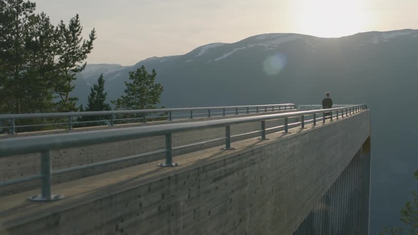 A person is standing in the distance on a bridge overlooking a mountain