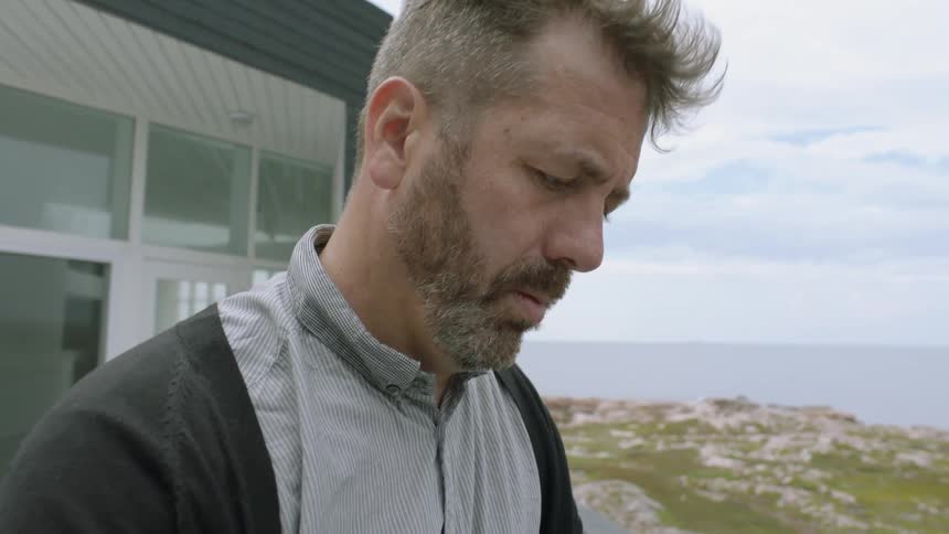 A man stands on his porch by the water