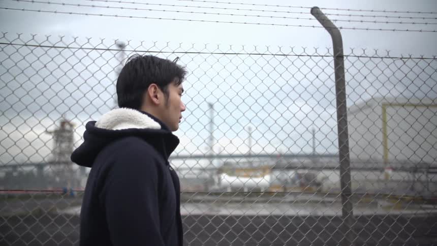 Man walking beside a fence on a cloudy day