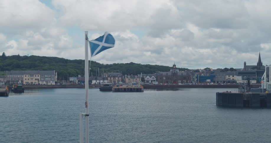 Scottish flag waves in front of a harbor with a town in the background