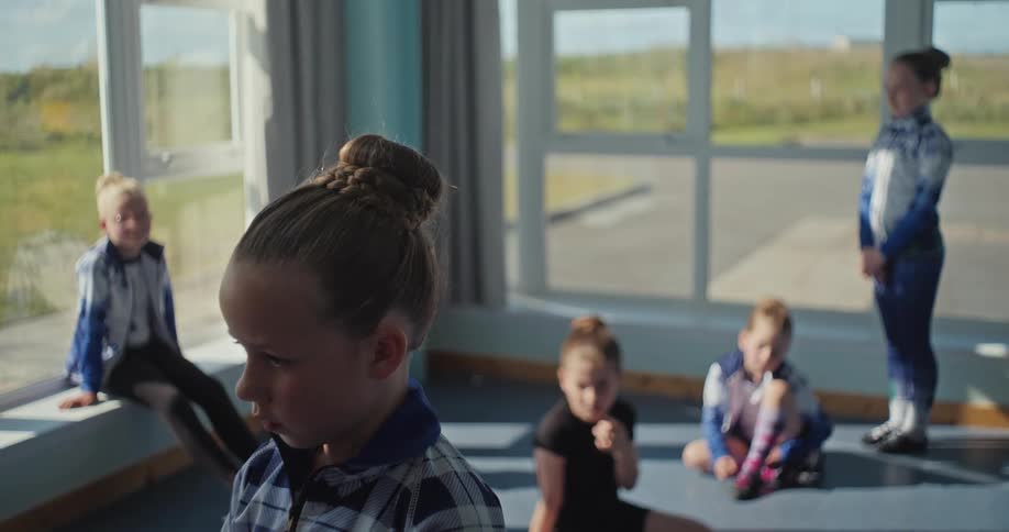 Children in scottish dance outfits rest and wait inside a room lit by large windows