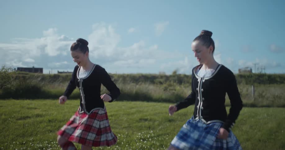 Two girls dance in a field moving their feet and legs in rhythmic patterns