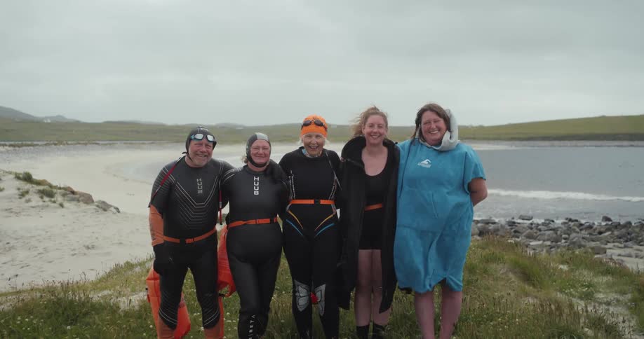 Group of people in open water swimming gear smiling on the beach