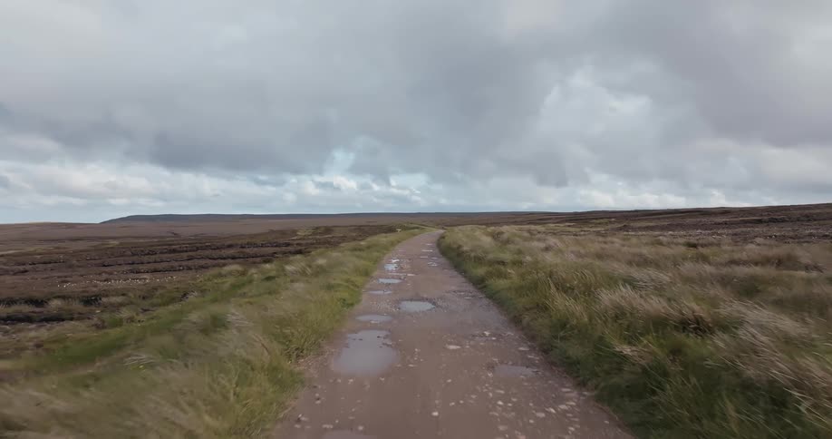 Landscape of a dirt road with potholes surrounded by a vast field on a cloudy day