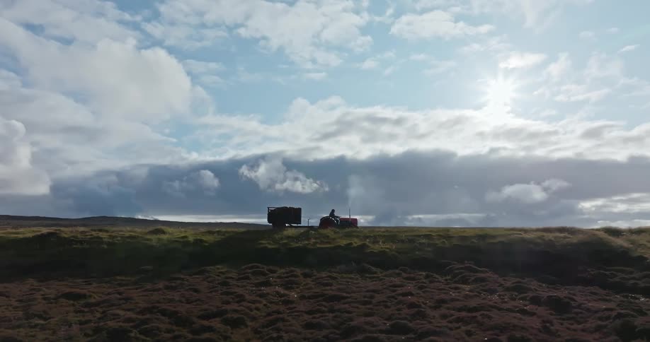 In the first clip a tractor is shown from a distance moving slowly across a vast grassy field under a cloudy sky the second clip features a person in a white spacesuit walking through a narrow hallway filled with an ominous red light