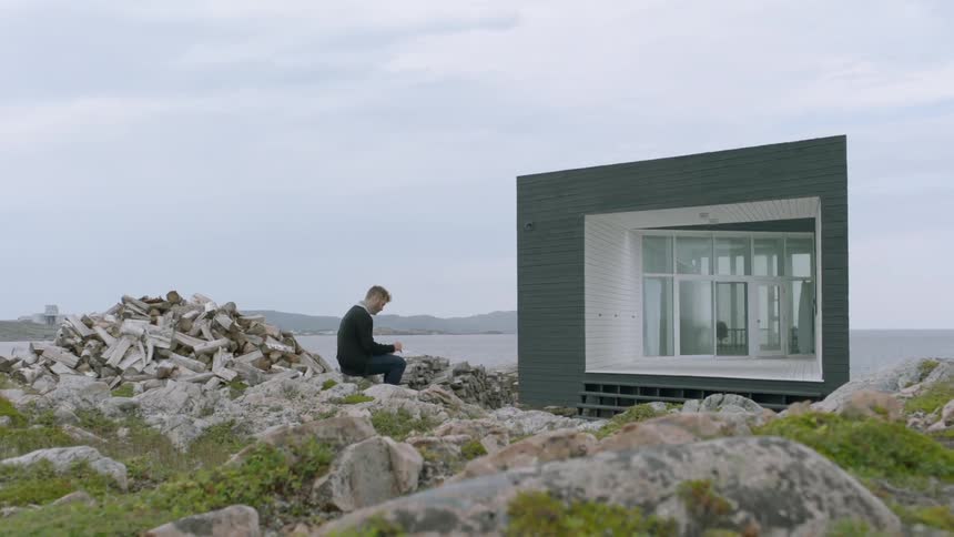 A man sits on rocks in front of a building