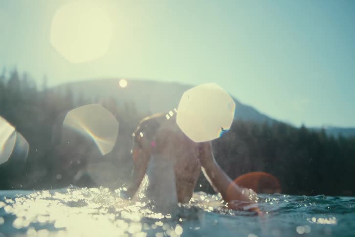 A woman is swimming in a forested lake on a sunny summer day