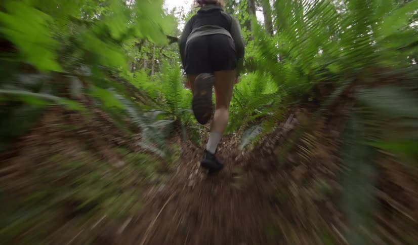 Woman running quickly along a trail surrounded by dense vegetation