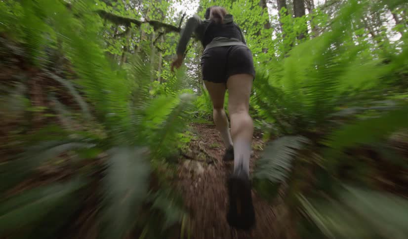 A person runs along a dirt path surrounded by trees and plants