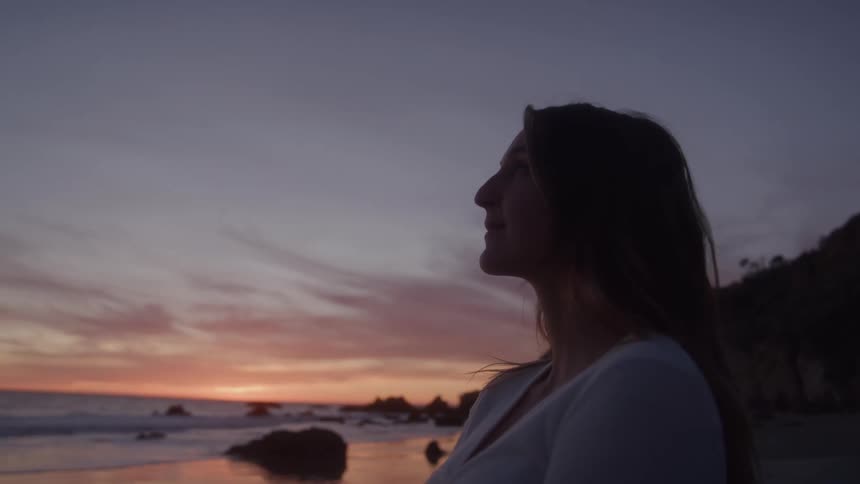 Woman gazing at the sunset by the sea in profile against the colorful horizon