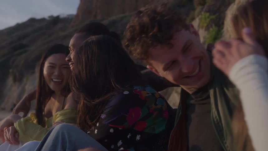 Group of friends sitting on the beach laughing together at sunset