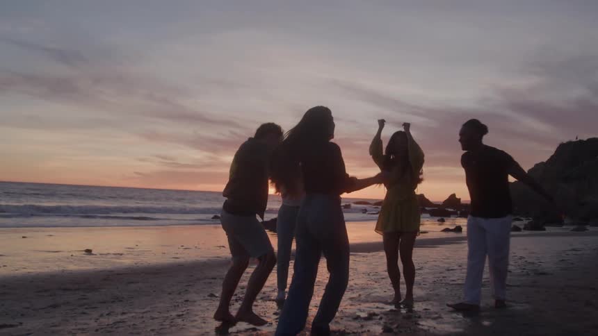 Group of friends having fun dancing on the beach in the late afternoon