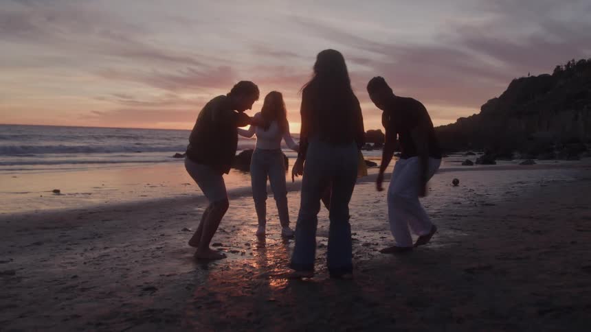 Group of friends dancing and having fun on the beach in the late afternoon