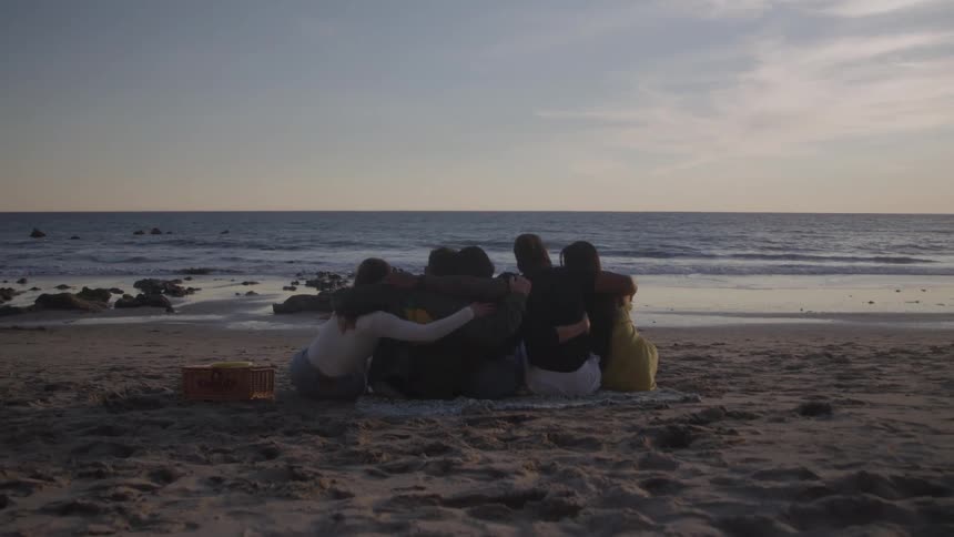 Friends hug while sitting on the sand
