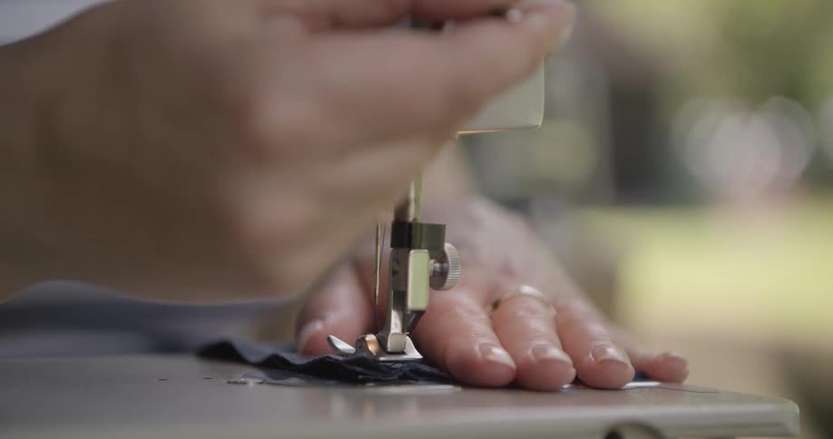 A persons hands one wearing a wedding ring carefully guide fabric through a sewing machine