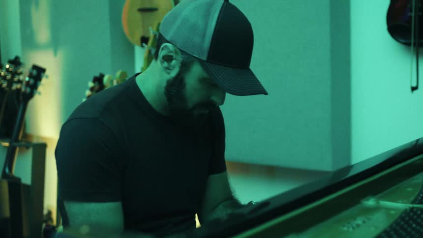 A man in a cap plays the piano in a dimly lit music studio