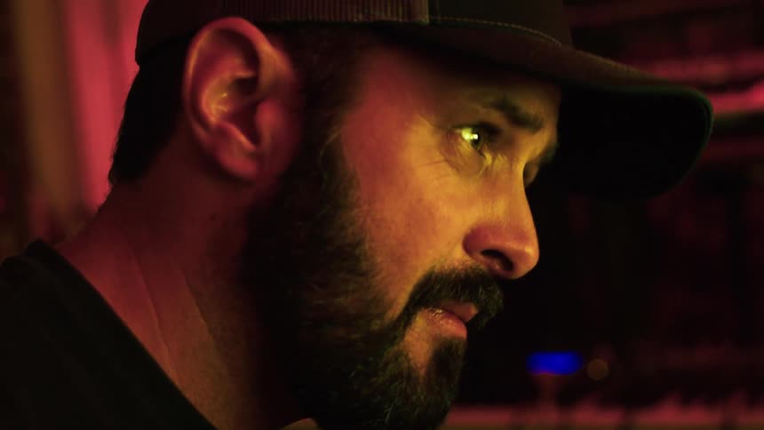 A man with a beard and a cap swinging his head on a indoor studio setting