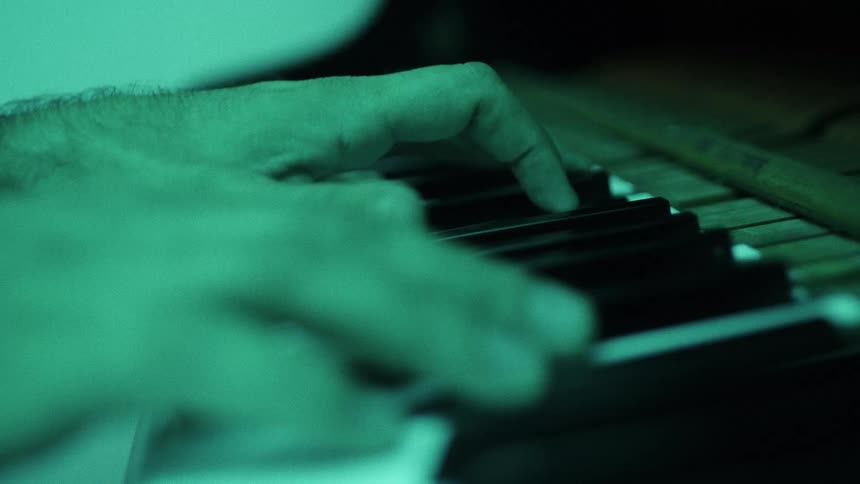 Closeup of hands playing piano keys under green lighting