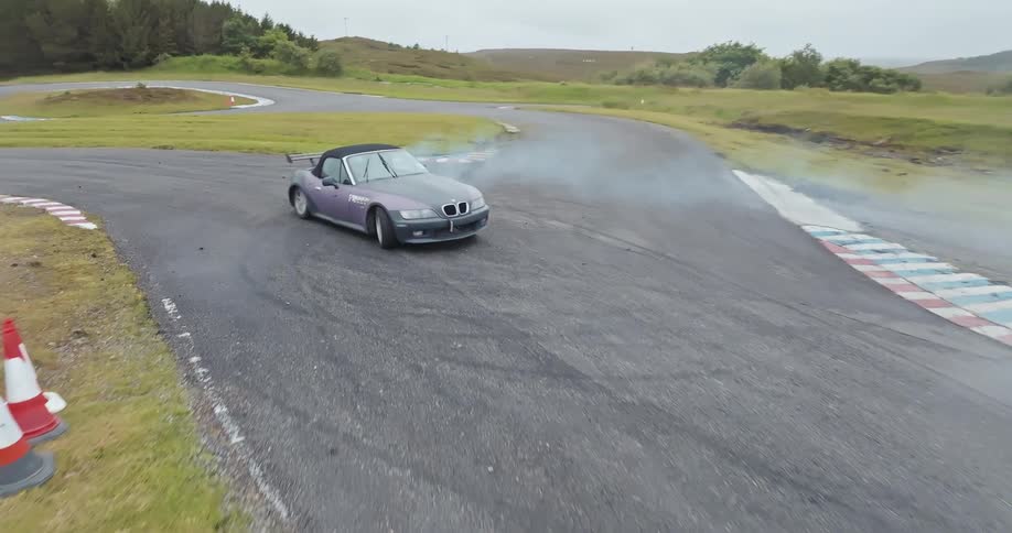 Sports car creates smoke while circling on a rural race track on a summer day