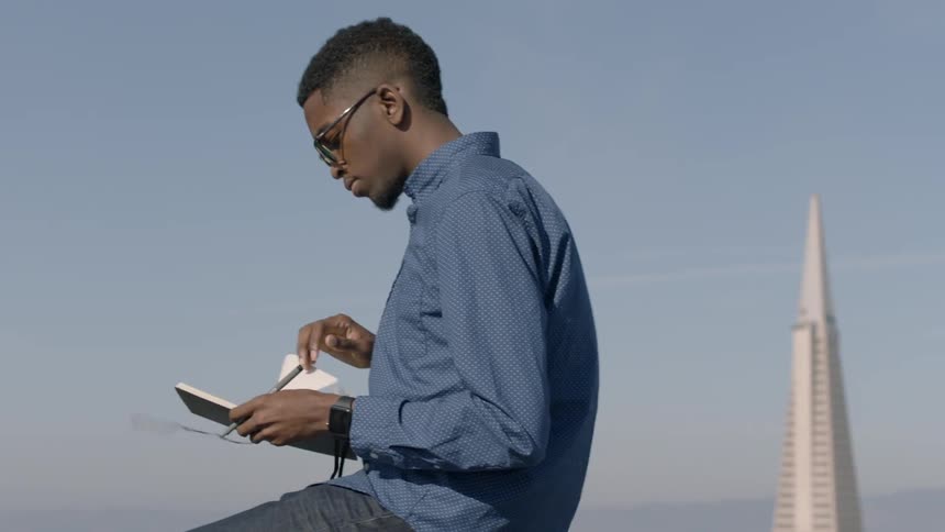 A man in a blue shirt writes in a notebook