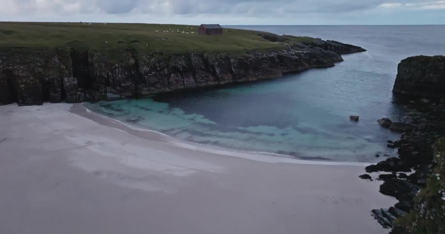 Lone house sits on a promontory while a bird flies over the beach near a seaside cliff