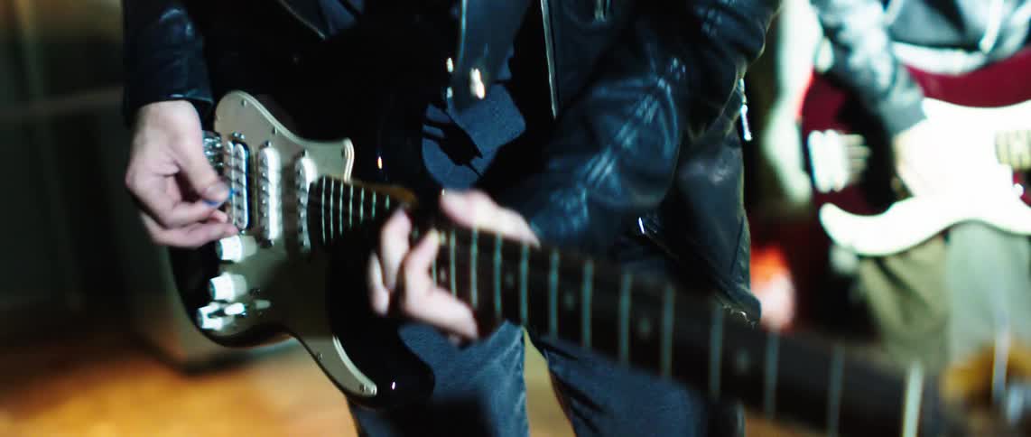 Two musicians strums an electric guitar during a live performance