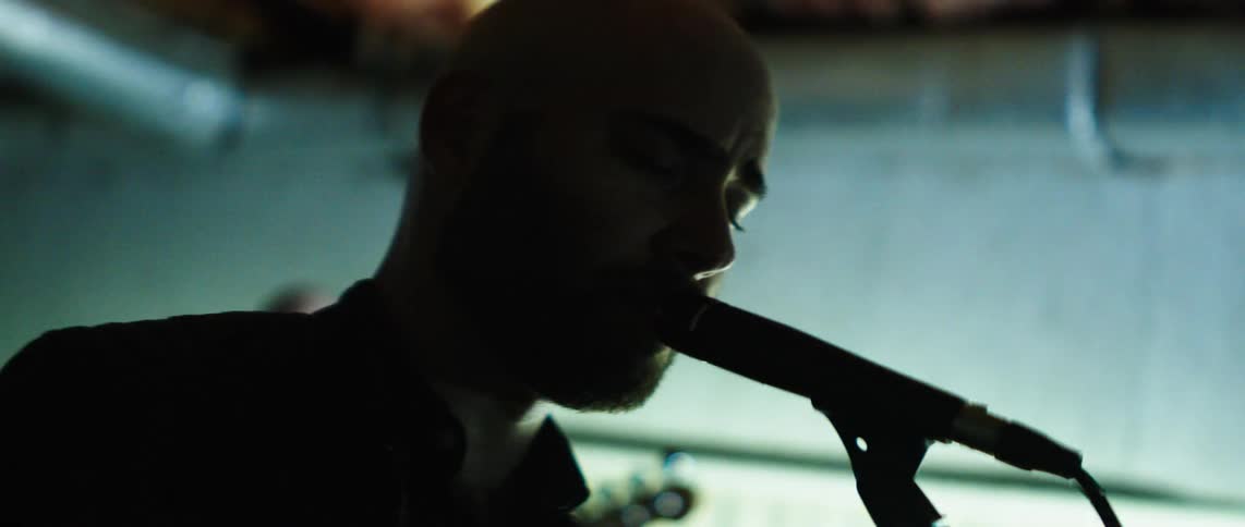 Bald man singing into a microphone