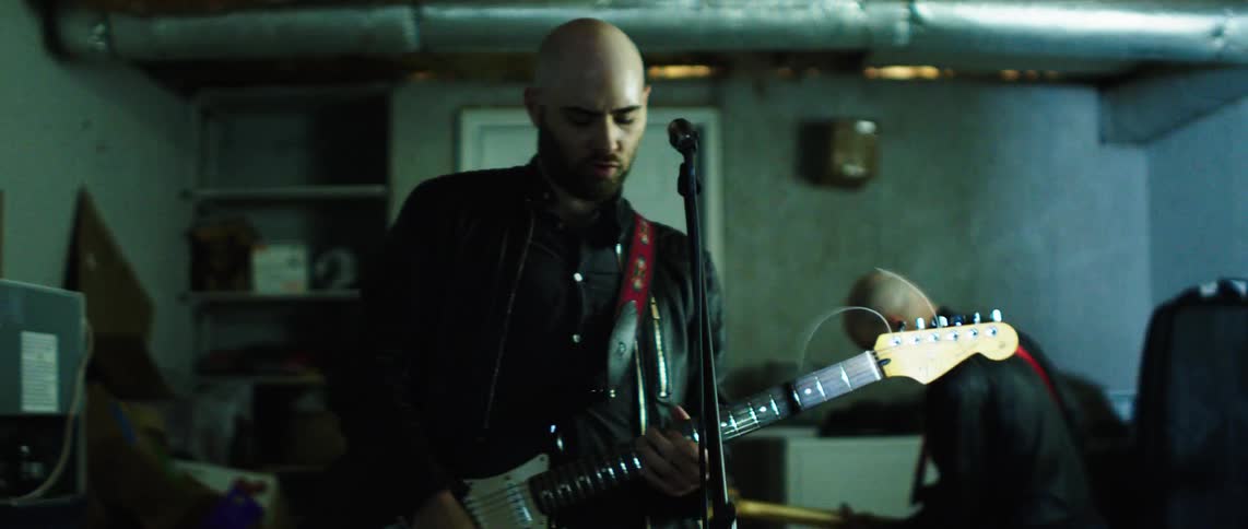 Musician plays an electric guitar and sings in a room with flashing lights