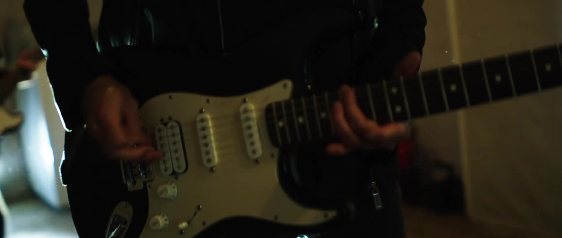 Guitarist standing in front of a microphone playswhile backlit by a spotlight