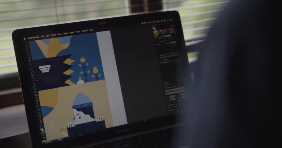 Person operating a laptop for graphic design while sitting beside a window