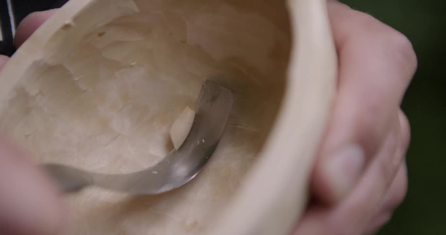 The man is carving a wooden bowl
