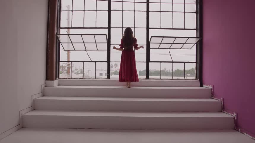 A woman walks barefoot up stairs toward large open windows