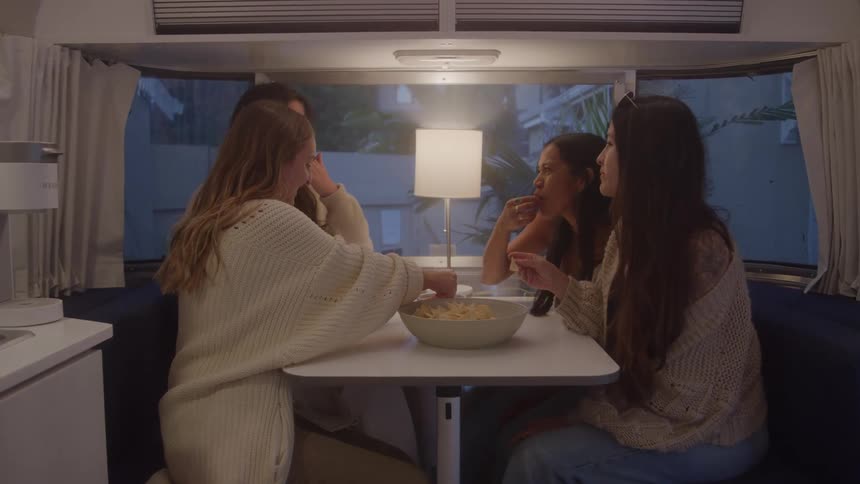 Four woman are sitting and having conversation on something and there are some food to eat on table