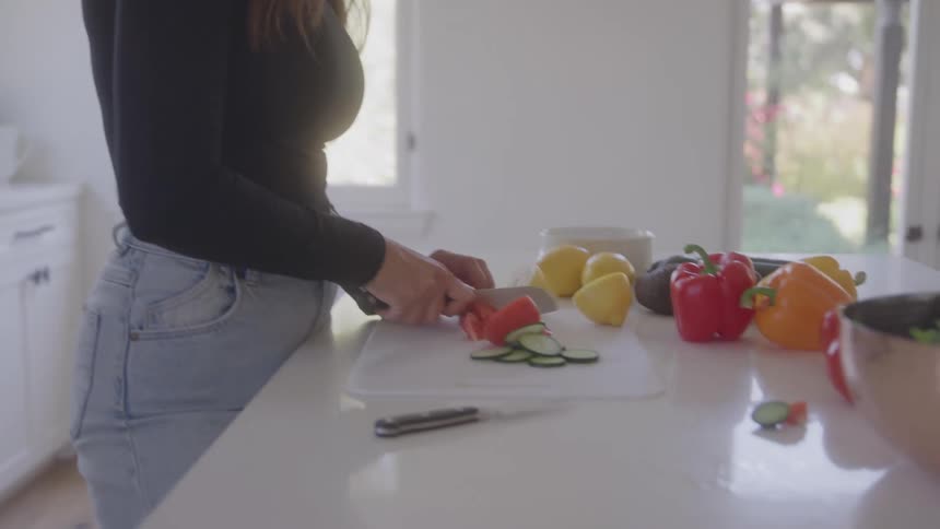 Woman slicing vegetables on a bright kitchen counter