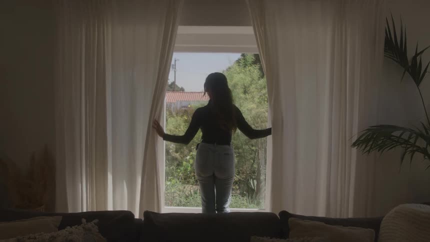 The woman opens the curtains in the living room