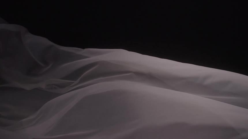 A close view shows a thin white sheet floating in the wind against a black background