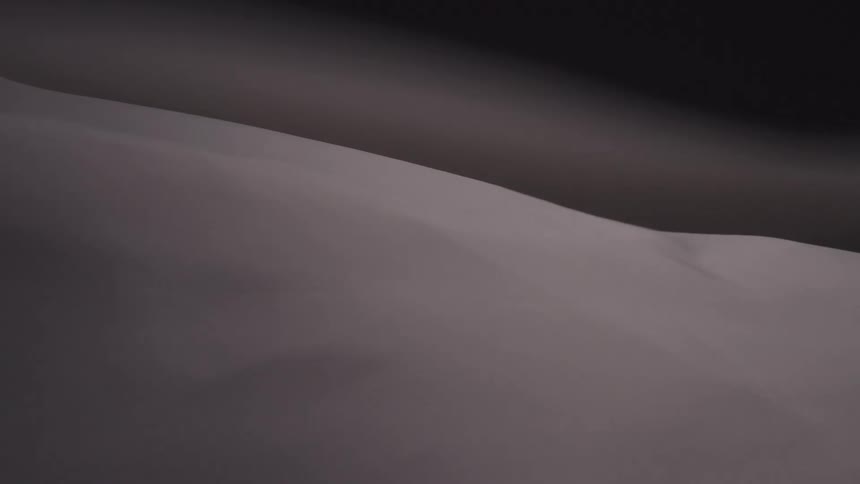 A close view shows a persons body covered with a thin white sheet against a black background